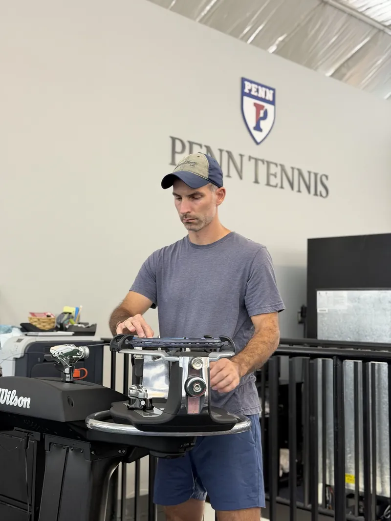 Mark Kuczynski stringing on site on a Wilson machine in front of the Penn Tennis backdrop