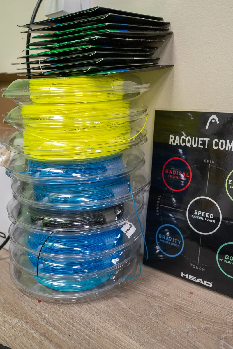A stack of Yonex string reels beside the Head racquet guide at URacquet Shop
