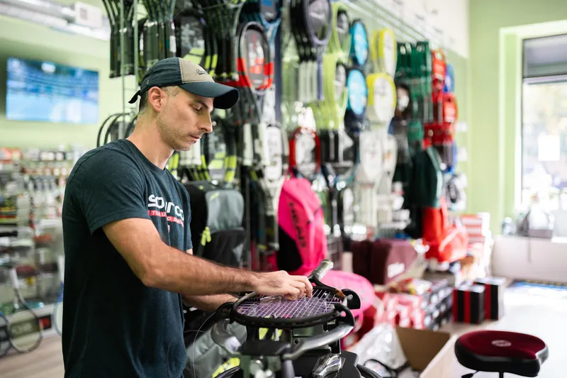 Mark Kuczynski stringing a racquet at URacquet Shop, with the racquet wall and the Pine Street windows behind him